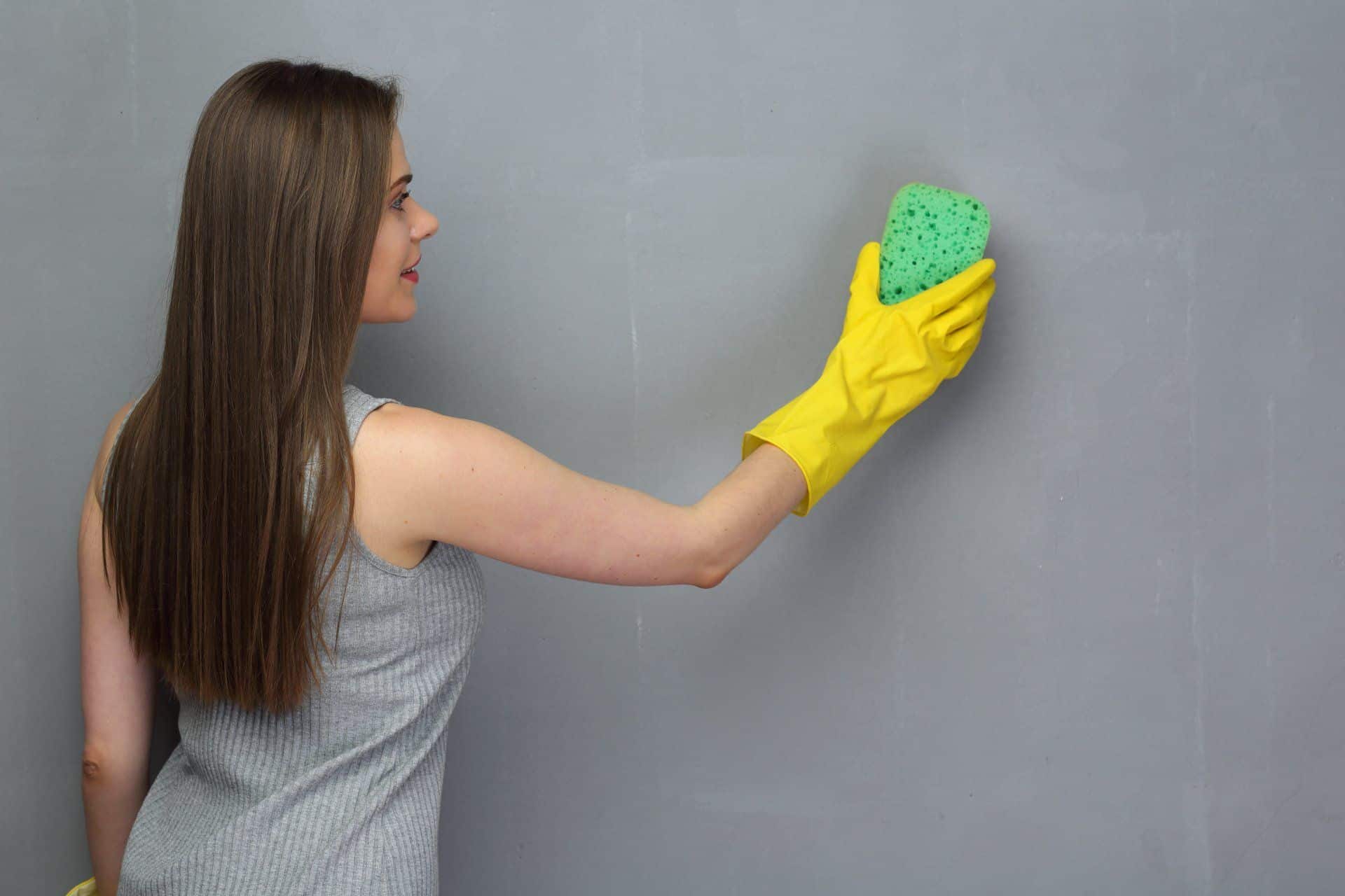woman using a sponge to clean a gray wall