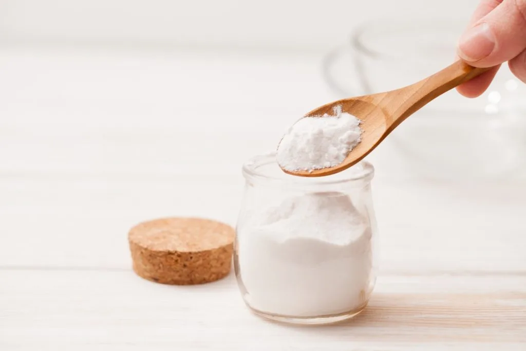 5 Tips to Beat Cabinet Grease Film in the Kitchen 19 Someone scooping baking soda out of a glass jar with a wooden spoon. Baking soda is a great way to clean grease off of kitchen cabinets.