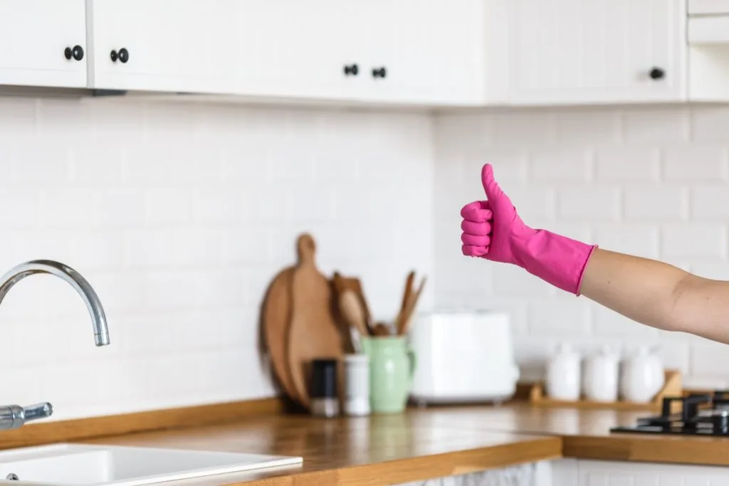 5 Tips to Beat Cabinet Grease Film in the Kitchen 22 Someone in a clean kitchen giving a thumbs up while wearing a pink rubber cleaning glove.