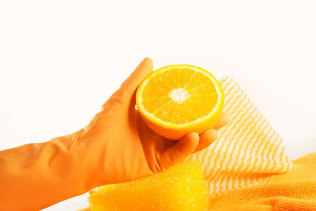5 Tips to Beat Cabinet Grease Film in the Kitchen 20 Someone in an orange cleaning glove holding an orange cut in half.
