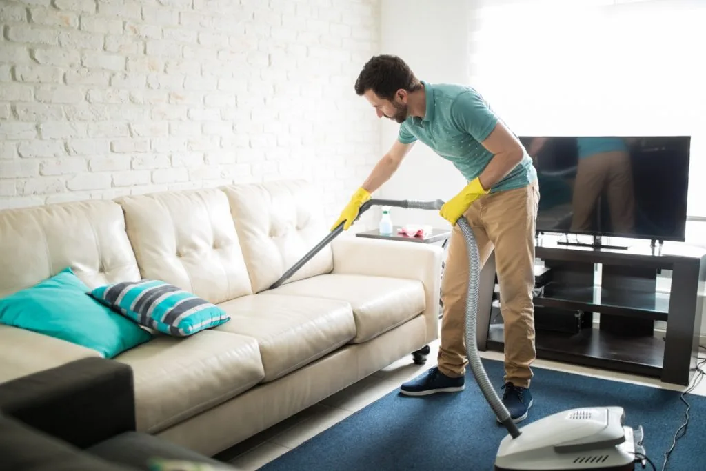21 Things in Your Home You Should be Throwing Out 13 A man using a vacuum to clean his couch. He is doing this after tossing Things in Your Home You Should be Throwing Out.