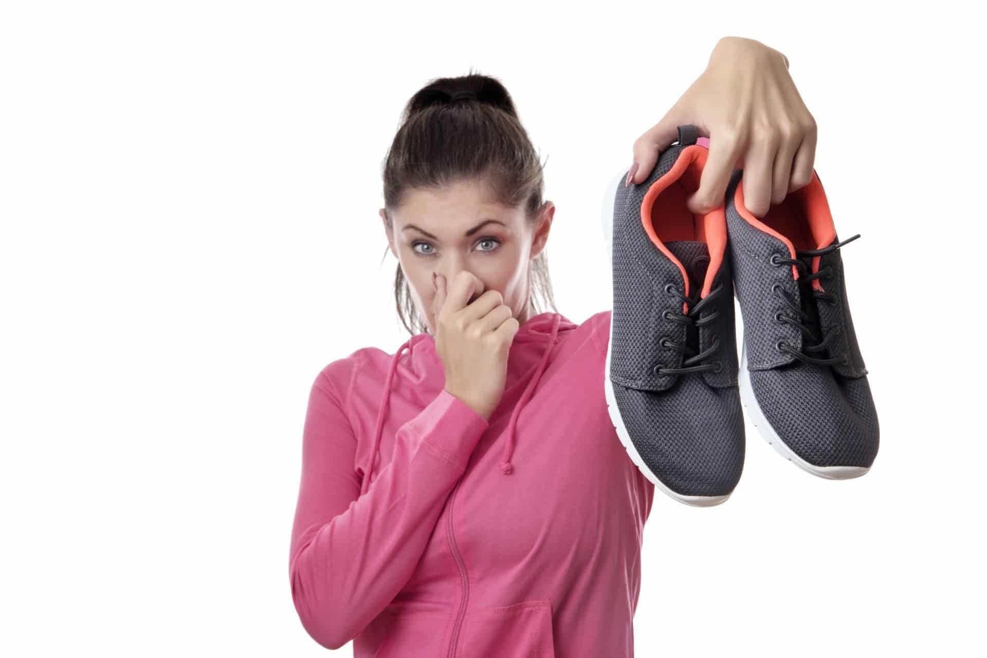 A woman holding her nose an a pair of old running shoes