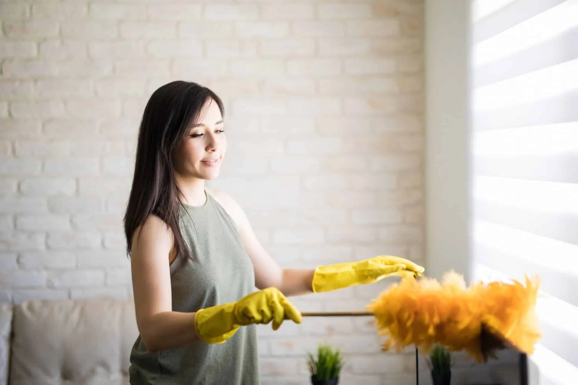 How Often You Should Really Be Dusting Your Home 3 woman using a yellow feather duster to dust her home