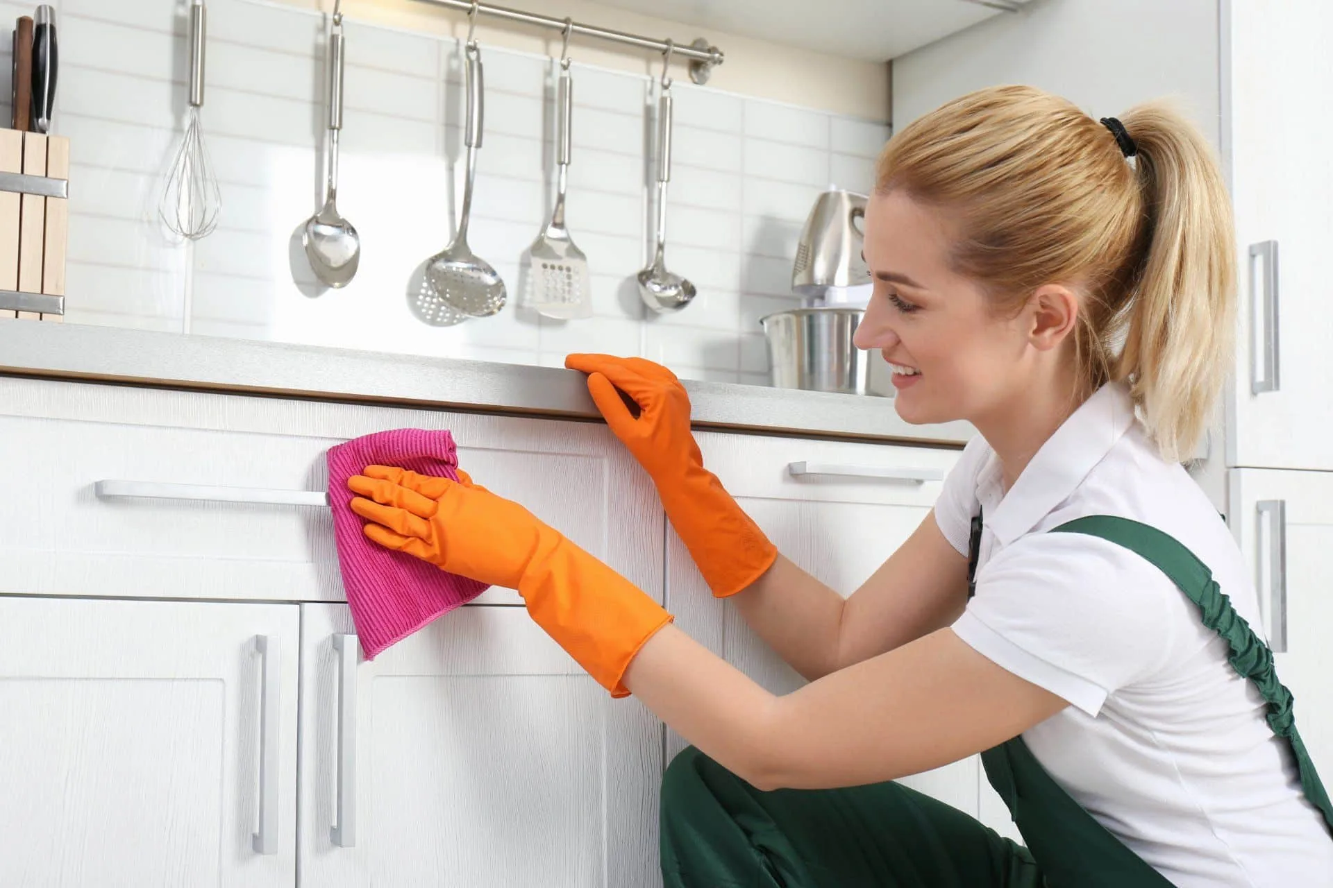 What You Should be Cleaning in Your Home Every Single Day 6 woman in orange cleaning gloves cleaning white cabinets