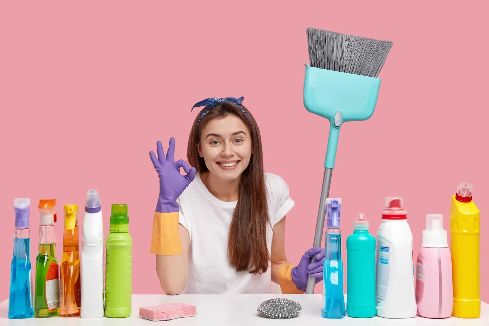 What's the Difference Between Cleaning, Disinfecting and Sanitizing? 15 a woman with cleaning supplies and holding a broom making the 'okay' sign with her hand