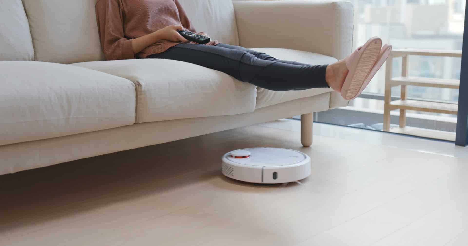 woman watching TV with her feet up while a robotic vacuum runs