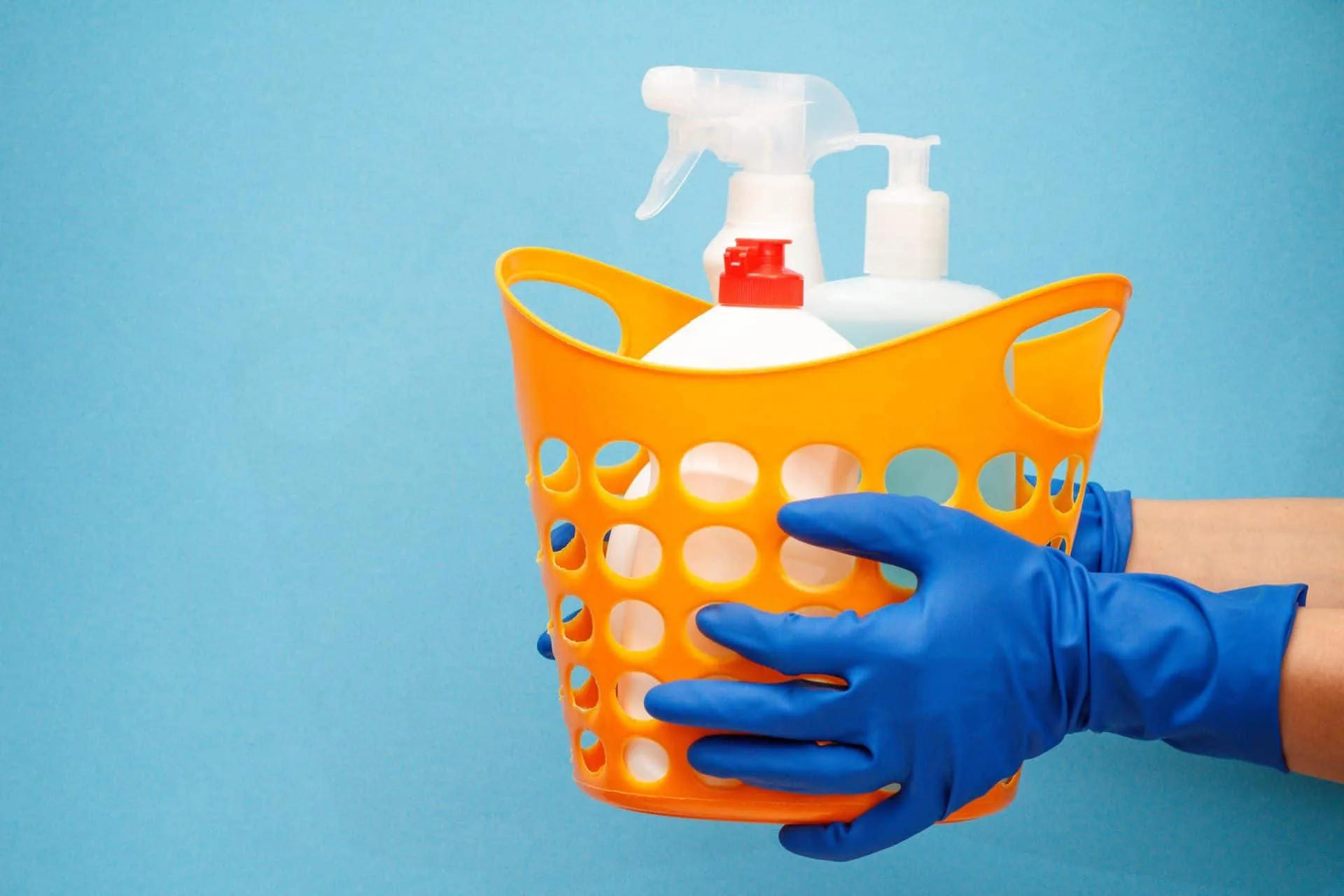 How to Clean Your House Using Bleach 3 person in blue gloves holding a basket of cleaning supplies