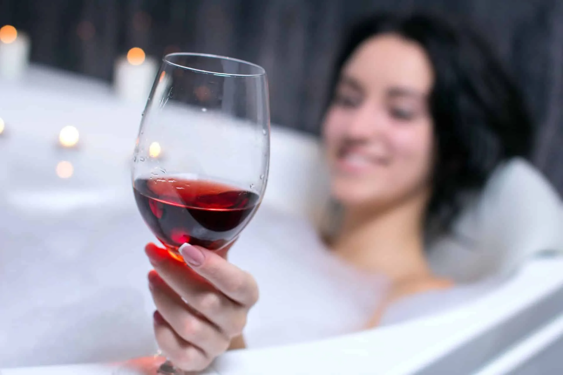 There is a Right Way to Scrub-A-Dub Your Tub 6 A woman enjoying a glass of red wine in a bath after learning about the best way to clean a bathtub.