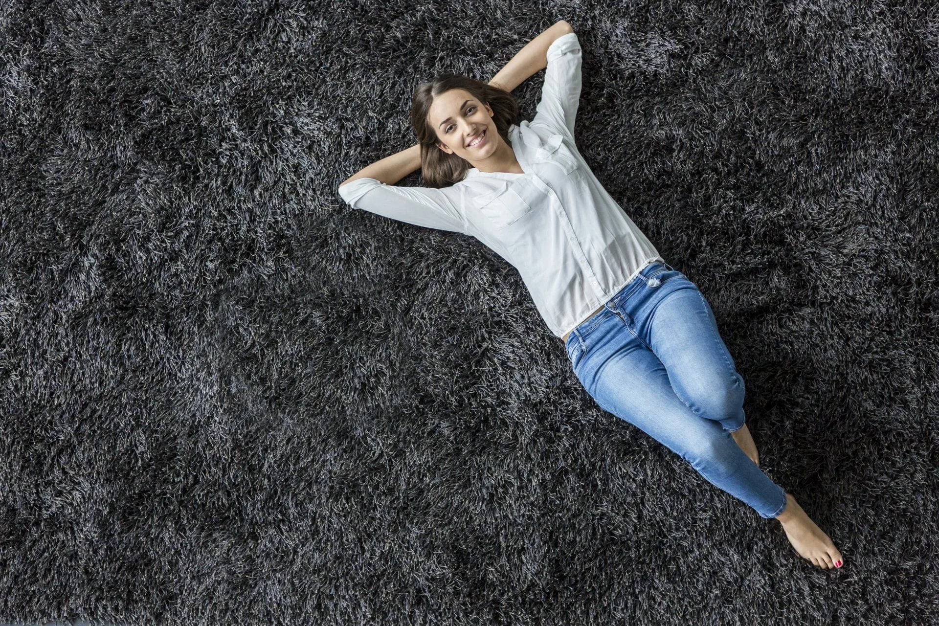 How to Care for Your Area Rugs 31 smiling woman laying on a dark gray shag rug
