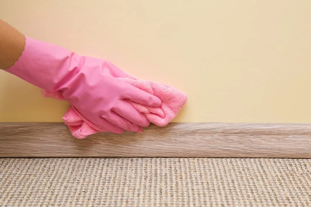 How to Clean Baseboards 12 Hand in rubber protective glove with microfiber cloth cleaning baseboard on the floor from dust at the wall. Early spring cleaning or regular clean up. Maid cleans house.