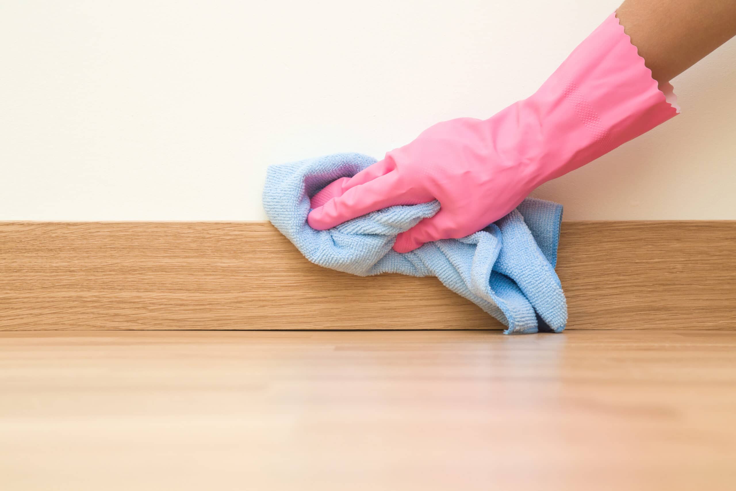 Someone wearing a pink glove cleaning baseboards with a microfiber cloth