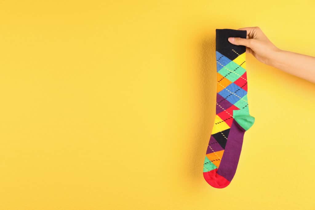 Woman holding bright sock and space for design on color background