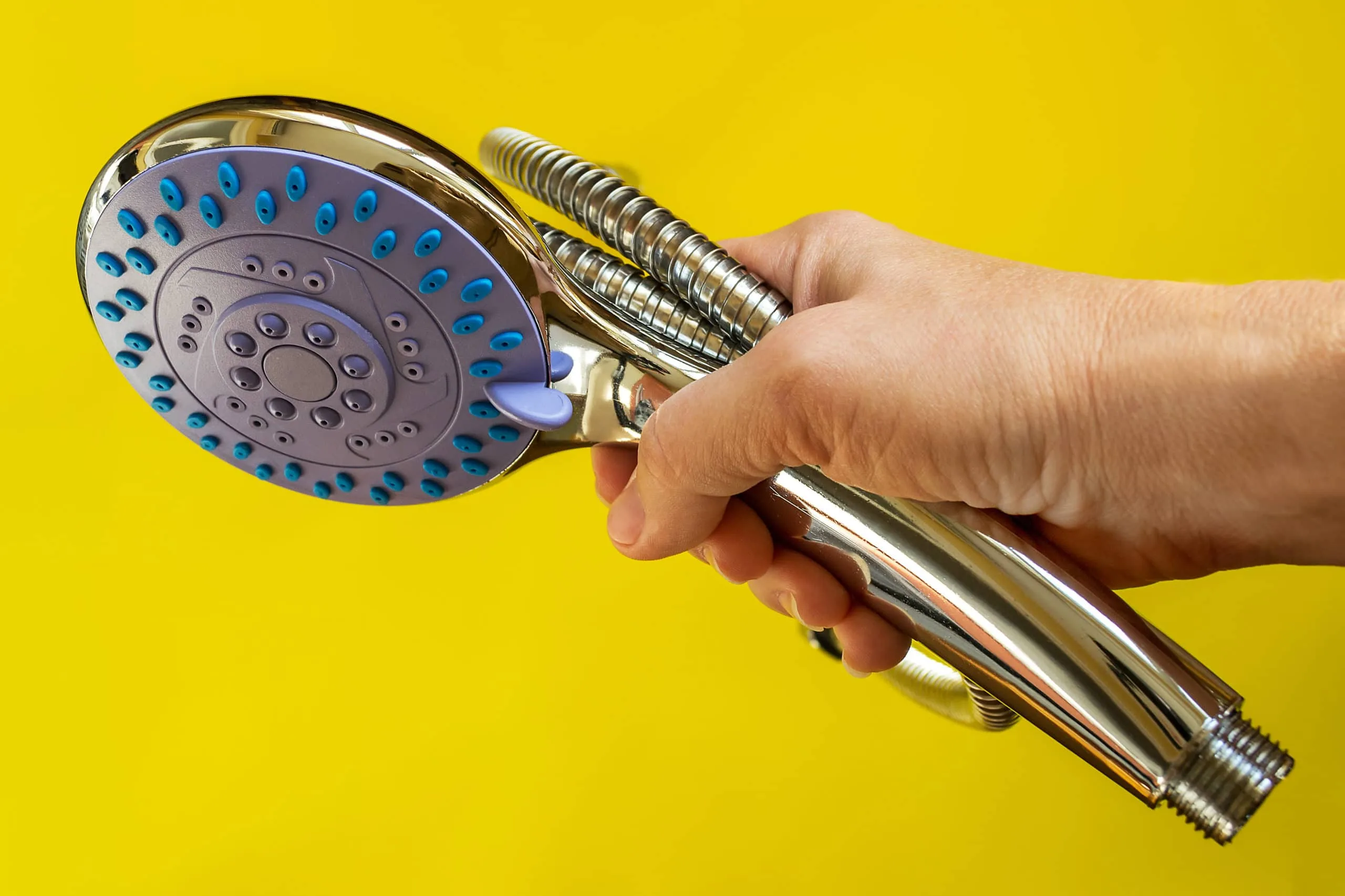 How to Clean a Shower Head 2 A person holding a showerhead on a yellow background