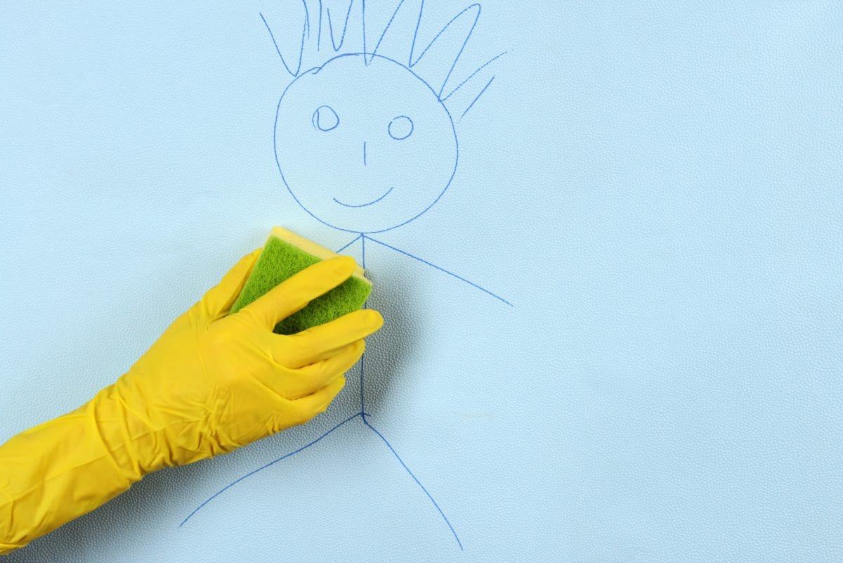 Someone wearing a yellow rubber cleaning glove using a sponge on crayon on the walls.