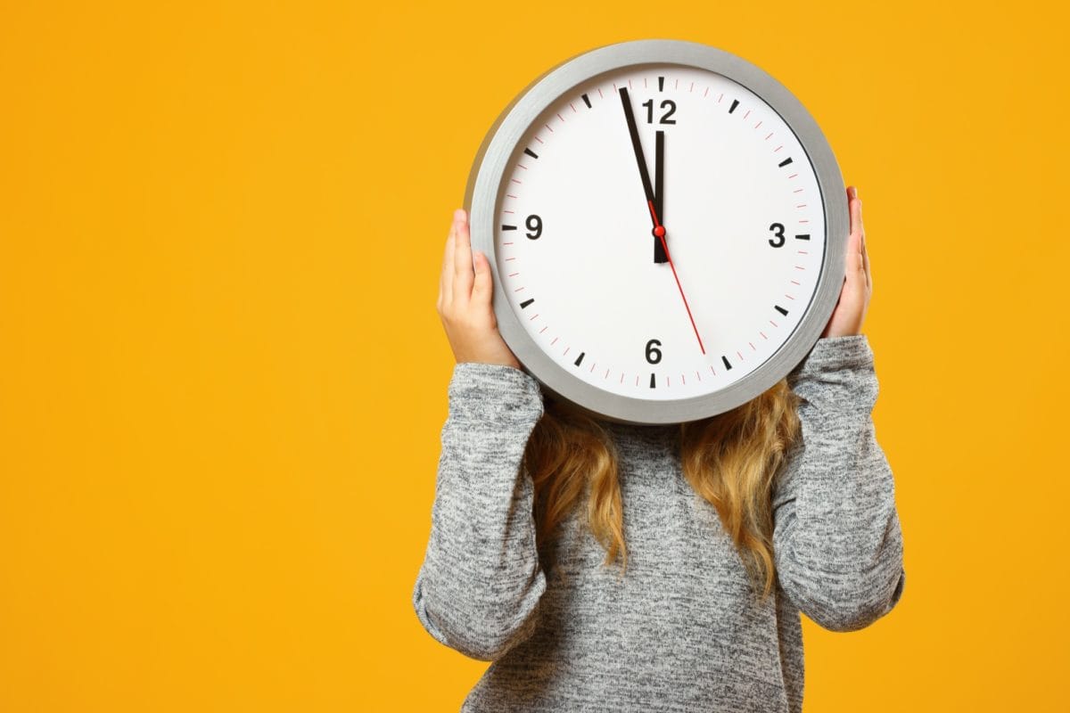 A women holding a large clock in front of her face symbolizing how to clean a room in 5 minutes.