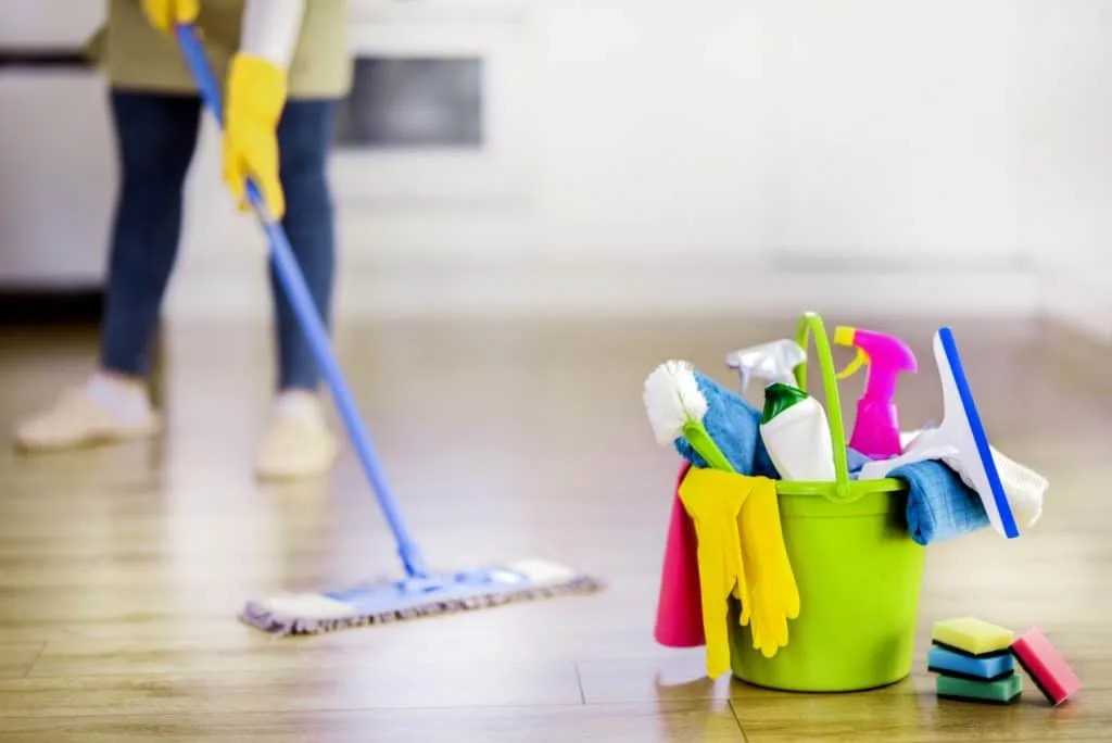 How to Clean Your House Cleaning Tools 3 A green bucket filled with house cleaning tools as someone mops in the background.