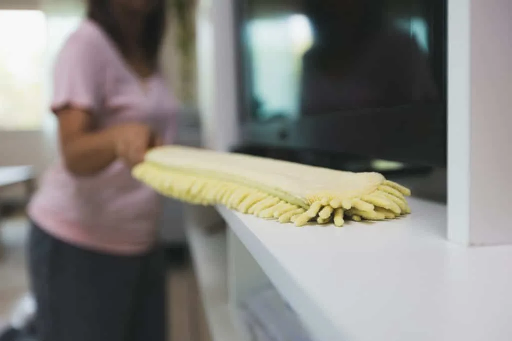 How to Clean Your House Cleaning Tools 7 A woman dusting with a yellow microfiber duster.