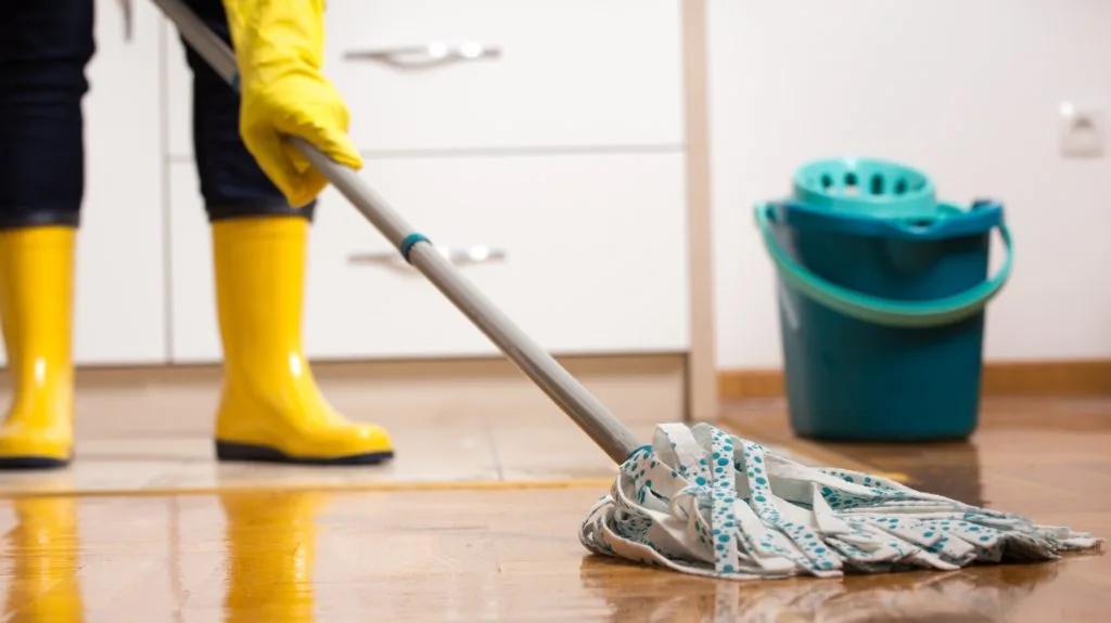 How to Clean Your House Cleaning Tools 4 Someone mopping in yellow cleaning gloves and yellow rain boots.