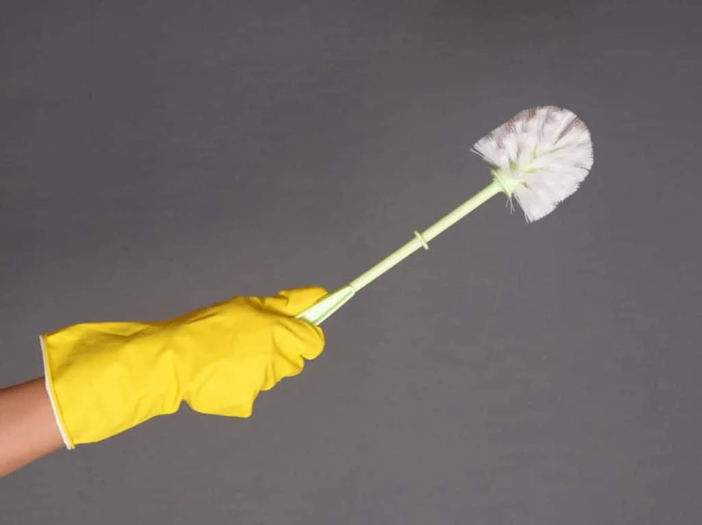 How to Clean Your House Cleaning Tools 6 Someone wearing a yellow rubber glove and holding a toilet brush.