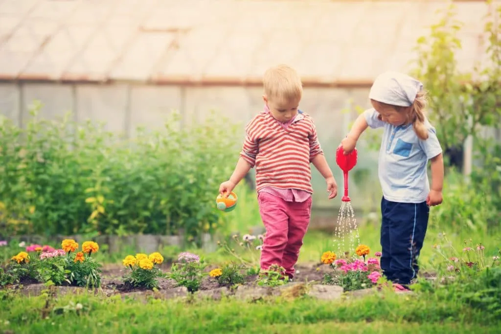 These 7 Chores for Kids Let You Delegate the Housework 6 Two small children watering flowers. Yard work is one of many great chores for kids.
