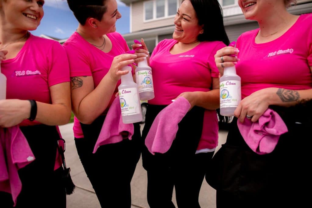 Four members of TLC Cleaning team wearing pink shirts and smiling while holding cleaning product spray bottles