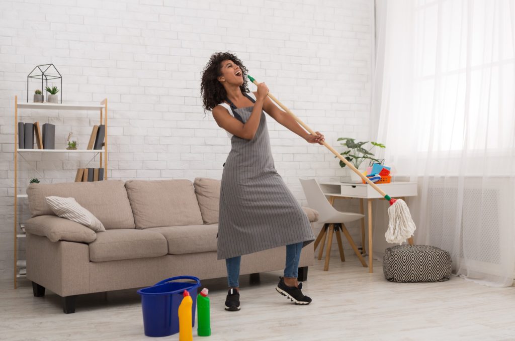 A woman singing into her mop handle while she cleans.