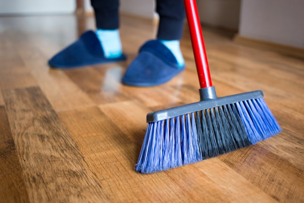 Someone wearing blue slipeprs and socks sweeping the floor. Sweeping is the first step of how to clean hardwood floors.