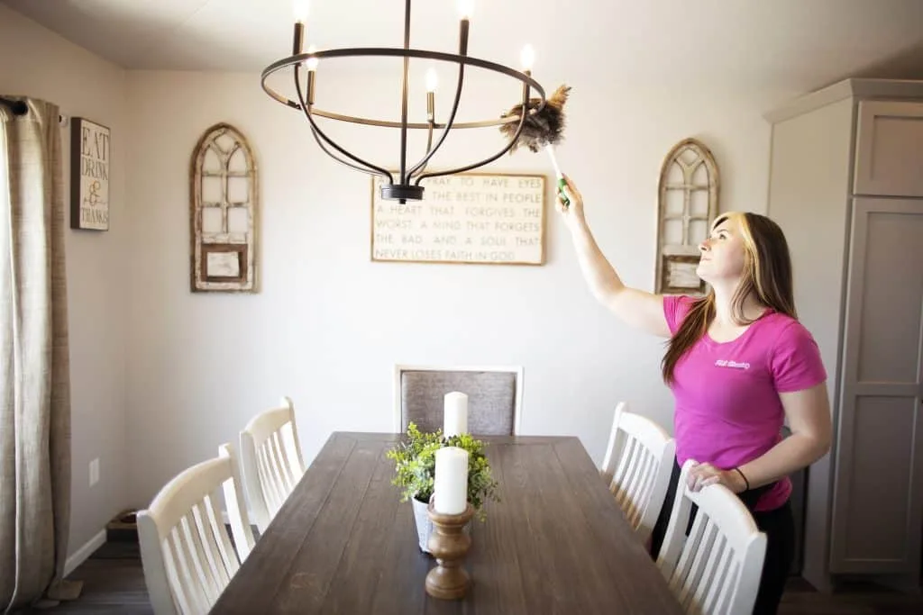 Move-In Cleaning: How to Start Fresh with a Spotless Home 1 A cleaning professional dusting a chandelier in a dining room, ensuring every detail is spotless and ready for use.
