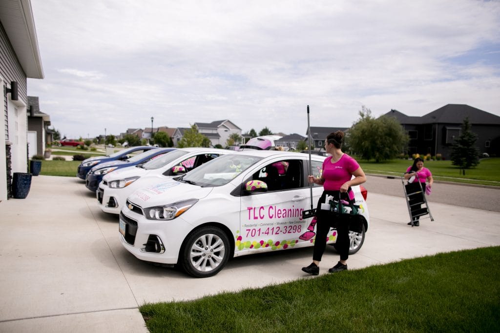 TLC Cleaning team members prepare for a new construction cleaning job, with branded vehicles and cleaning supplies ready in a residential neighborhood.